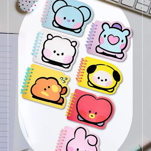 A set of BT21 Miniel memo note pads with cute cartoon character designs, arranged on a white oval plate over a desk background with a keyboard, pen, and glasses.