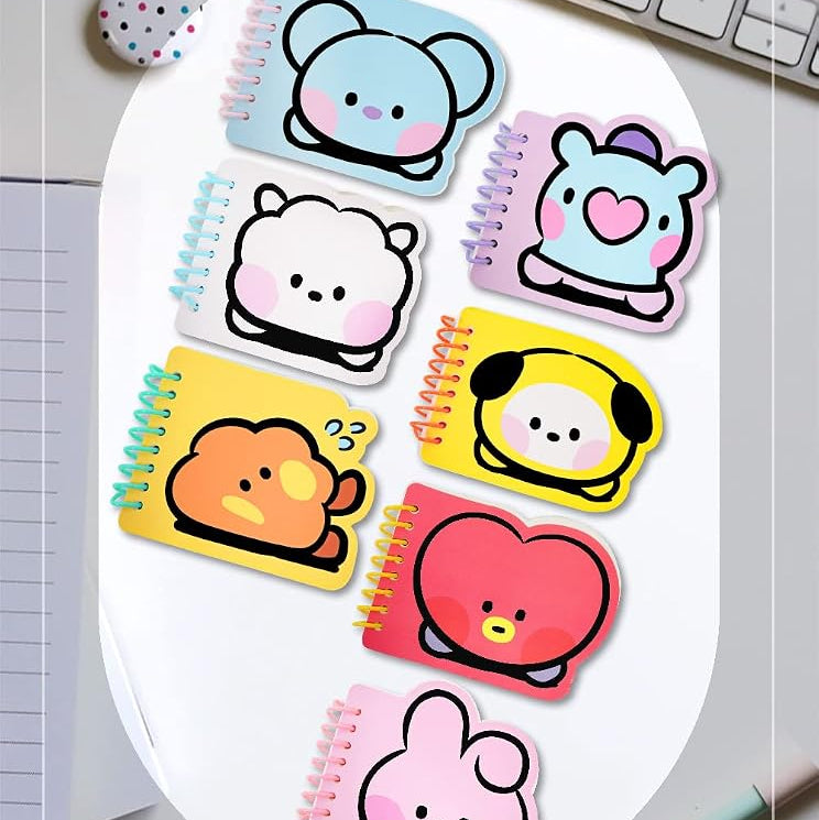 A set of BT21 Miniel memo note pads with cute cartoon character designs, arranged on a white oval plate over a desk background with a keyboard, pen, and glasses.